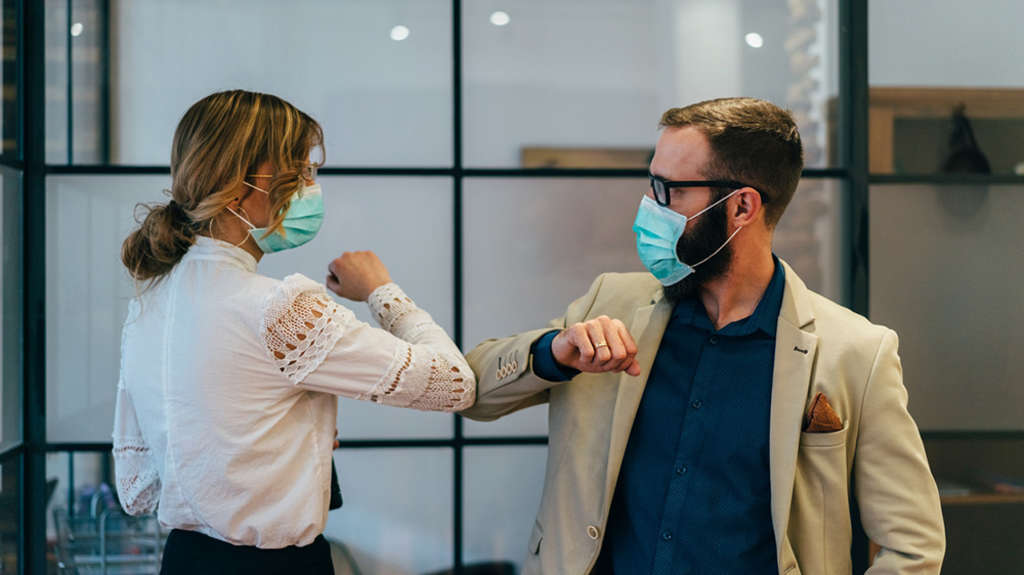 two business people with face masks greeting one another by bumping elbows